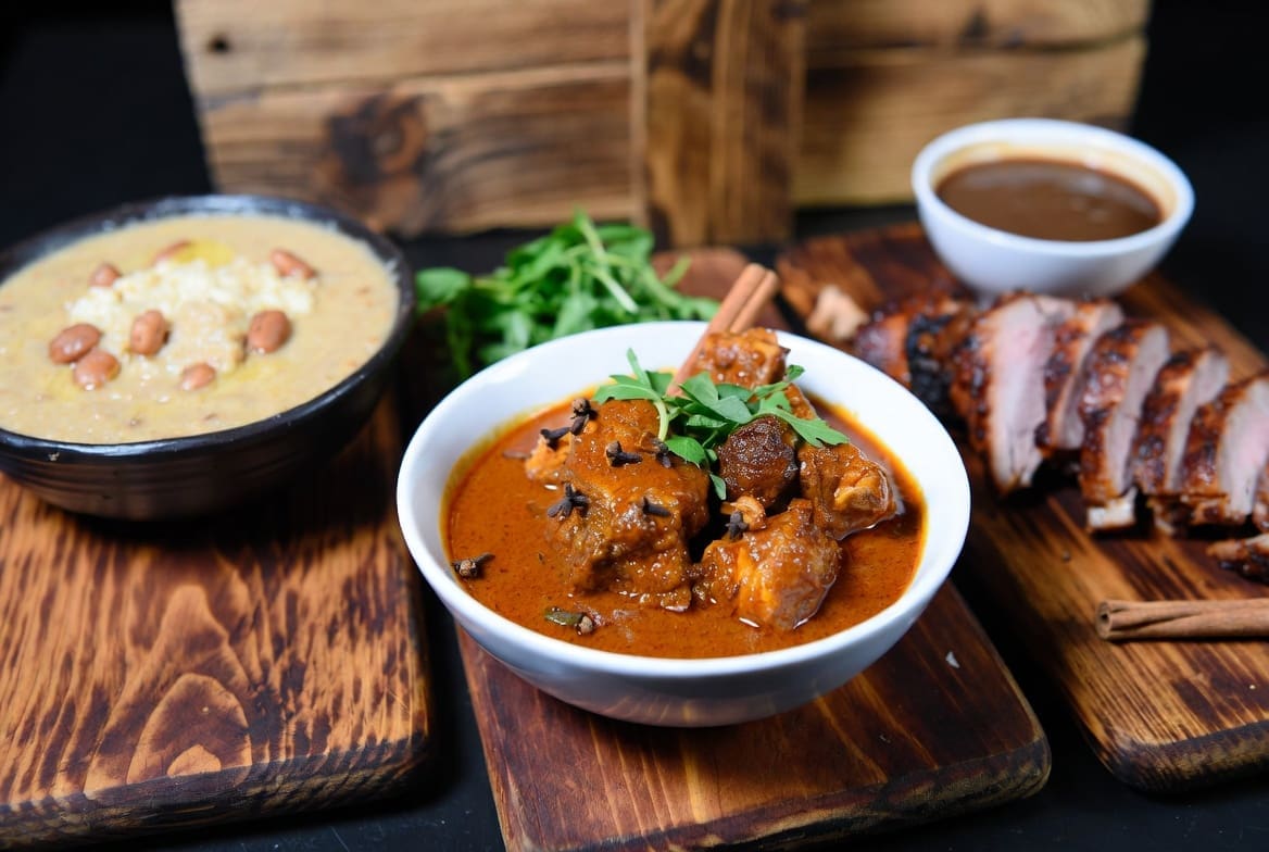 Traditional South African dishes showing different cultures in South Africa and their food – samp and beans, Cape Malay style curry, and sliced spit-roasted meat